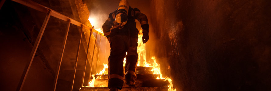 A firefighter ascends a flaming stairwell