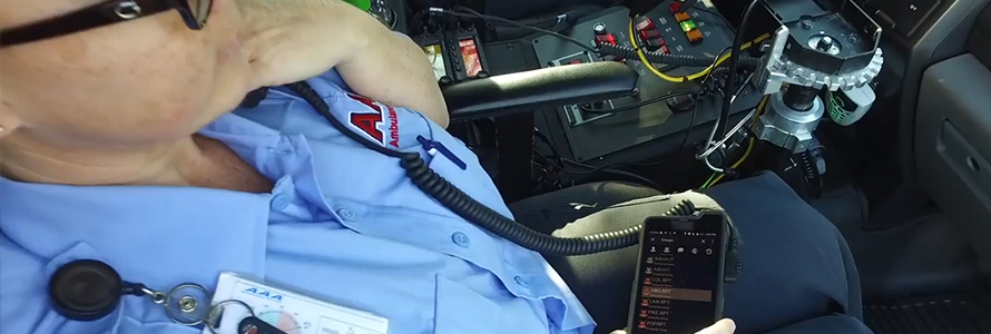 An emergency medical practitioner sits in an ambulance, speaking into a radio handset connected to a cell phone. An emergency medical practitioner sits in an ambulance, speaking into a radio handset connected to a cell phone.