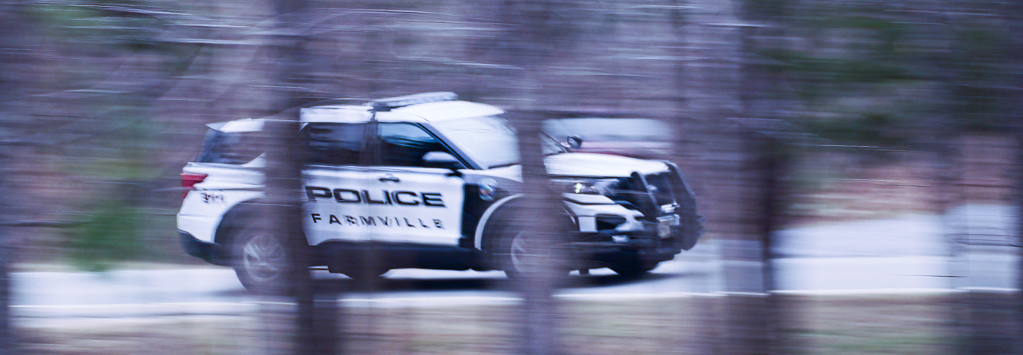 A Farmville Police Department sport utility vehicle driving down the road, captured through the trees.