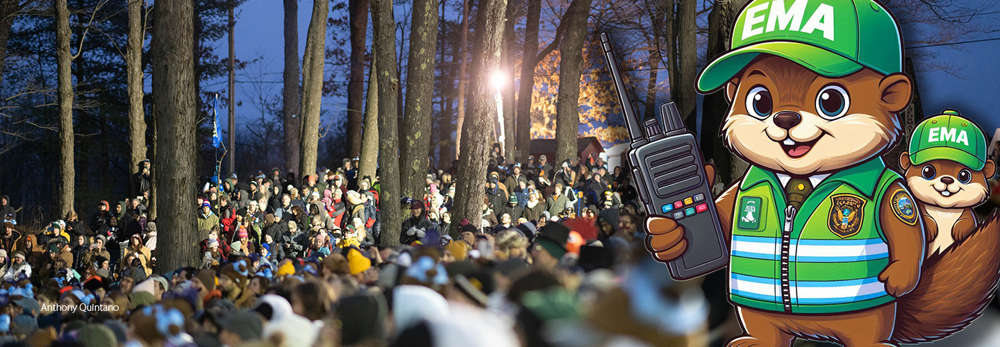A group of people gathered in a wooded area attending the annual Groundhog Day ceremony. A cartoon image of groundhogs dressed as emergency management officials with one holding a mobile device.