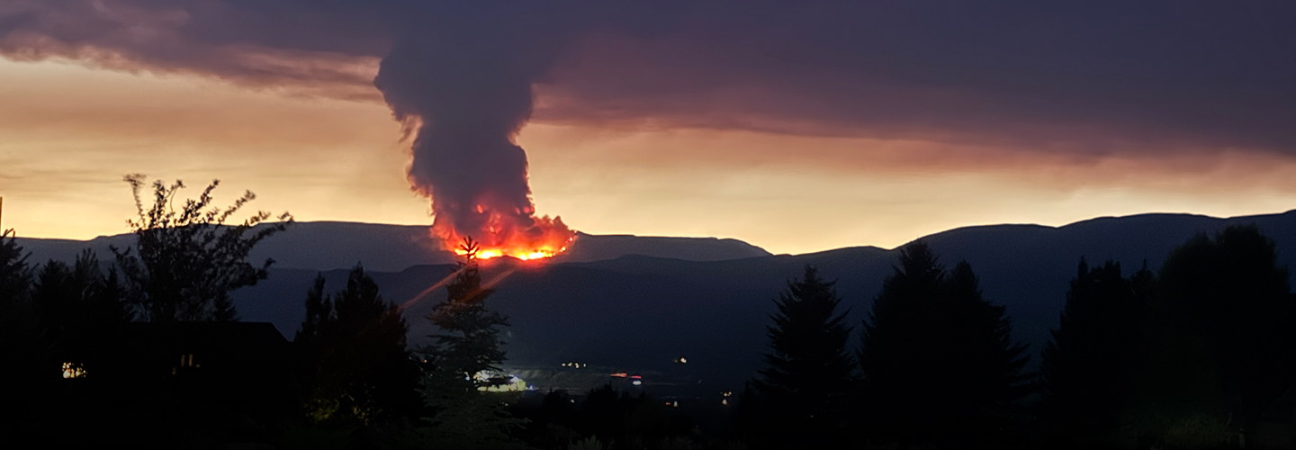 The Derby Fire burning on a distant mountain obscuring most of the sky with smoke while clouds in background are illuminated by the fire. 