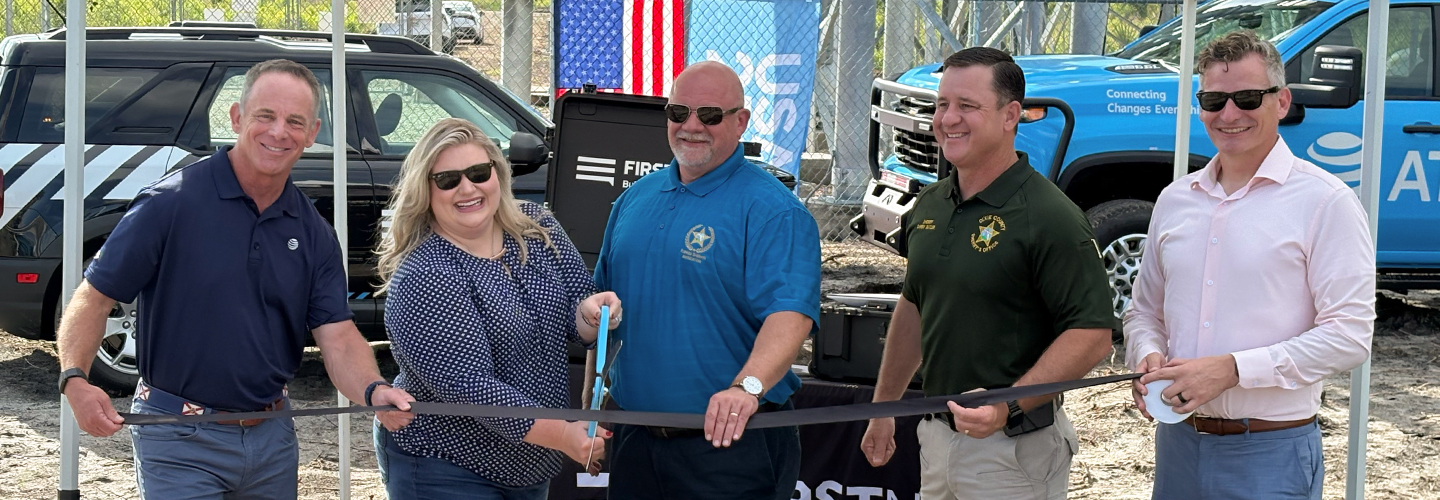 AT&T SE President Joe York, U.S. Representative Kat Cammack, FirstNet Authority Board Chairman Sheriff Adkinson, Dixie County Sheriff Darby Butler, and AT&T President of FirstNet & Public Sector Mobility Scott Agnew standing under a FirstNet by AT&T tent, holding a ribbon and large scissors for a ceremonial event launching a new cell tower in Horseshoe Beach, Florida