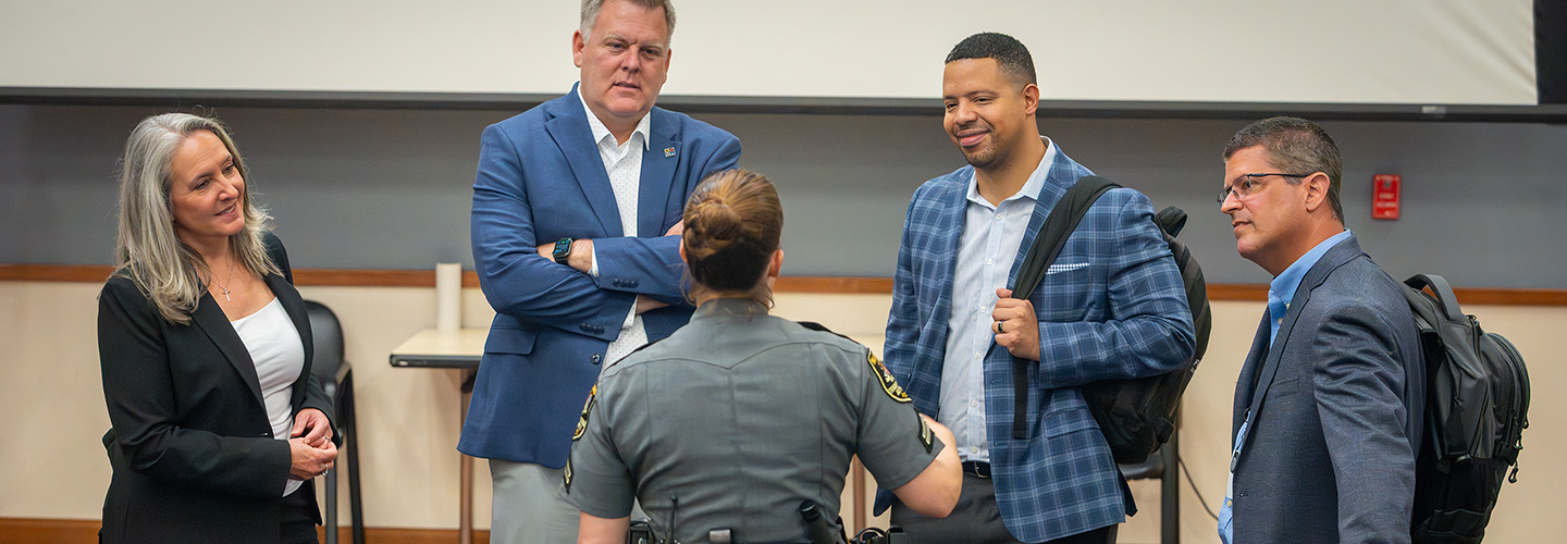 FirstNet Authority staff and Coverage Enhancement Workshop participants, including a uniformed law enforcement officer, stand in a circle speaking