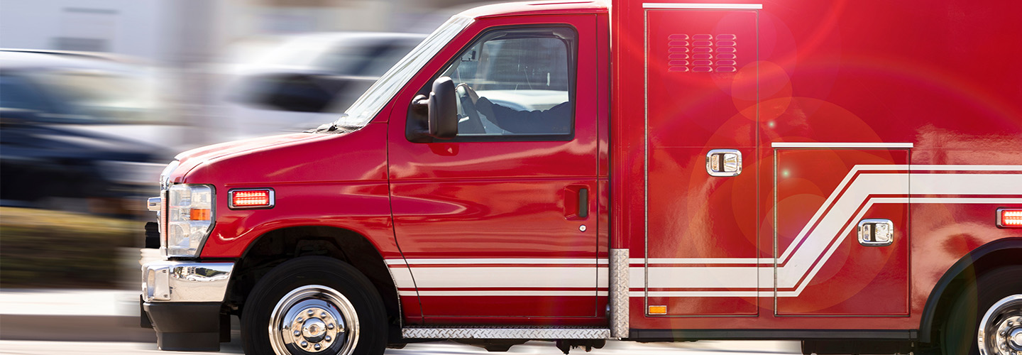 Red ambulance in motion with blurred road in background.