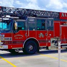 Two trucks in a parking lot on a cloudy day; a fire truck emblazoned with “Altoona Fire Department”; a FirstNet SatCOLT with “FirstNet Build With AT&T” on the side. 