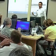 Episode 71: Emergency Planning for Natural Disasters: Redefining Readiness in Macon-Bibb, Georgia Emergency Manager addresses group of individuals including military uniformed men gesturing urgently.