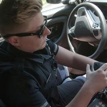 A police officer holds a radio and works on a mobile data computer while sitting in a patrol car.