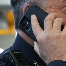 A law enforcement officer with a shoulder mic talking on a smartphone
