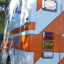 A brightly painted ambulance sits parked on the side of a rural road surrounded by many trees.