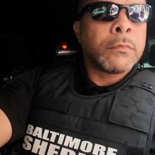A Baltimore sheriff’s deputy driving a patrol vehicle with one hand on the steering wheel