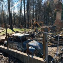 A VW bug sits inside the ruins of a burned down house and garage.