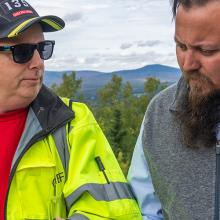 FirstNet Authority public safety advisor Bruce Fitzgerald talks with Jackman-Moose River Fire Chief Bill Jarvis with the mountains of Maine in the background during autumn