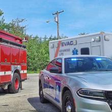 A police officer using a tablet stands in front of a fire truck, police car and ambulance.