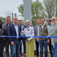 Lake Lure Ribbon Cutting FirstNet Authority Executive Director and CEO Michael Cannon stands with federal, state and local leaders in front of a new cell tower with a blue ribbon in front. The mayor in the middle stands ready with scissors to cut the ribbon.