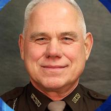 Sheriff Neil A. Miller and background of plaque for the Chief Harlin R. McEwen Public Safety Broadband Communications Award