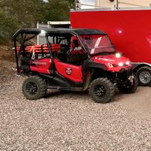 A truck, UTV, and transport trailer outfitted with FirstNet devices such as HPUE parked outside a Northwest Fire and Rescue station. 