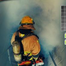 A firefighter in safety gear with a tank on his back descends stairs into a smoke filled area. 