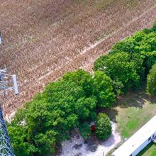 Aerial view of the top of a FirstNet cell site tower with a field and grove of trees in the background. Aerial view of the top of a FirstNet cell site tower with a field and grove of trees in the background.