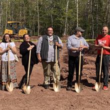 Thirteen people stand with gold shovels, ready to break ground on a cell tower at Red Cliff Reservation