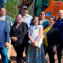 Eleven representatives who broke ground at a cell tower on the Red Cliff reservation stand in front of an excavator.