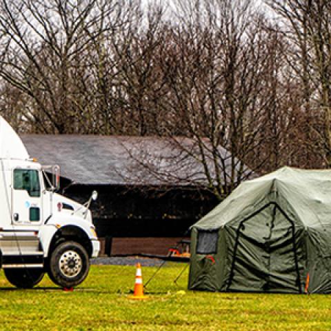 An AT&T SatColt and a tent are set up in a field near a forest. 