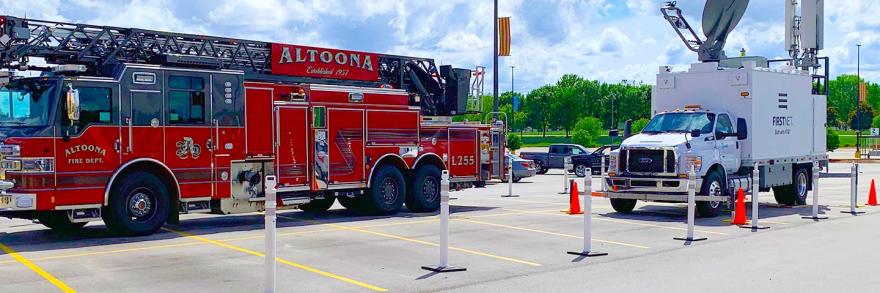 Two trucks in a parking lot on a cloudy day; a fire truck emblazoned with “Altoona Fire Department”; a FirstNet SatCOLT with “FirstNet Build With AT&T” on the side. 