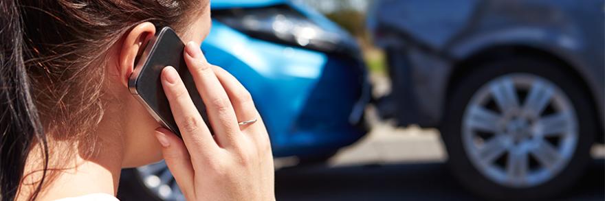 A woman making a phone call in front of a fender bender.