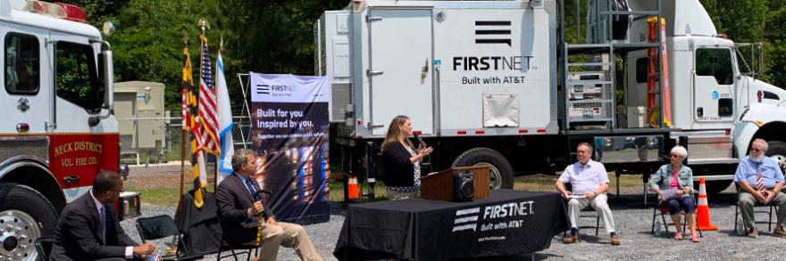 Public safety stakeholders; FirstNet Authority and FirstNet, Built with AT&T, staff; and state politicians sit in front of a fire truck and a deployable satellite truck.