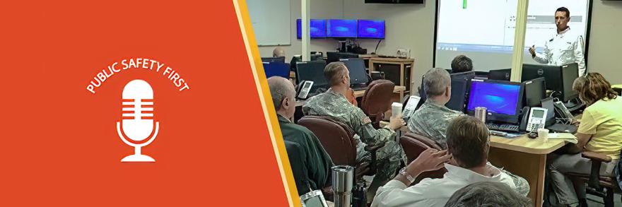 Emergency Manager addresses group of individuals including military uniformed men gesturing urgently.   