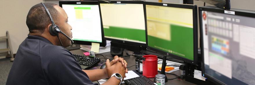 An emergency dispatcher sits in front of an emergency response system with his headset on.