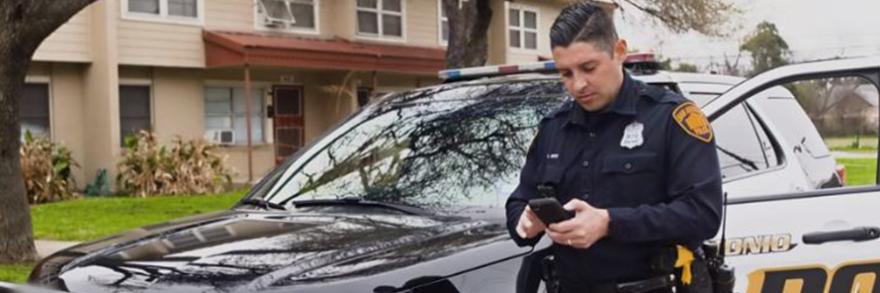 San Antonio Police officer near his car looking at a cell phone
