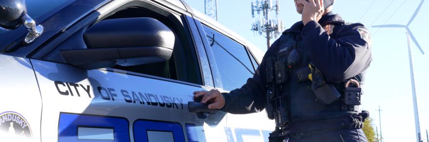 A Sandusky police officer speaks on a FirstNet phone near his patrol vehicle