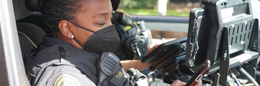 Two University of Maryland, Baltimore campus police officers checking out a laptop in the front of their parked cruiser