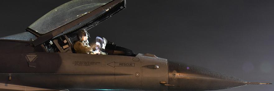 Air Force pilot sits in a jet at night.