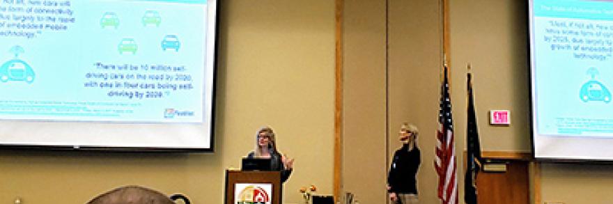 A woman stands behind a podium on a stage giving a presentation.