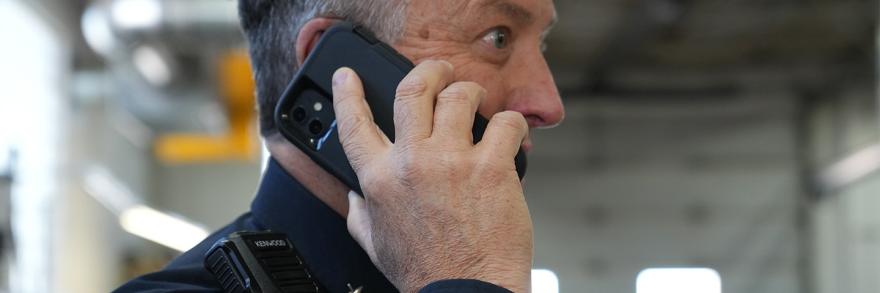 A law enforcement officer with a shoulder mic talking on a smartphone