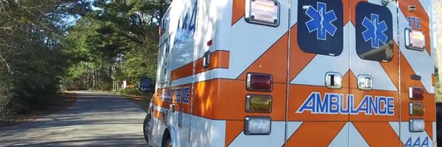 A brightly painted ambulance sits parked on the side of a rural road surrounded by many trees.