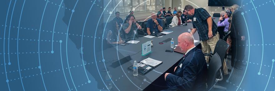 Attendees gather around a table at the FirstNet Users Summit; abstract pattern moves outward from attendees like rings on a tree 