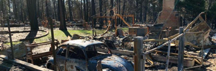 A VW bug sits inside the ruins of a burned down house and garage.