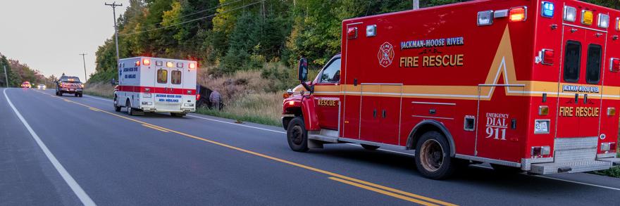 Ambulance and other vehicles from the Jackman Moose River Fire Rescue agency responding to a vehicle accident in a ditch beside a rural road. 