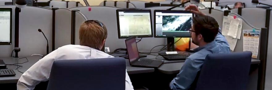 Two public safety officials look at multiple computer monitors at a workstation