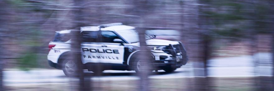 A Farmville Police Department sport utility vehicle driving down the road, captured through the trees.