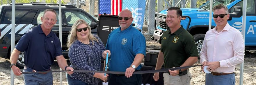 AT&T SE President Joe York, U.S. Representative Kat Cammack, FirstNet Authority Board Chairman Sheriff Adkinson, Dixie County Sheriff Darby Butler, and AT&T President of FirstNet & Public Sector Mobility Scott Agnew standing under a FirstNet by AT&T tent, holding a ribbon and large scissors for a ceremonial event launching a new cell tower in Horseshoe Beach, Florida
