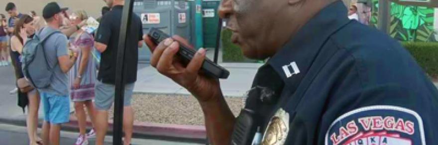 A City of Las Vegas Fire and Rescue uniformed officer speaks into a smartphone. Behind him are music festival attendees.