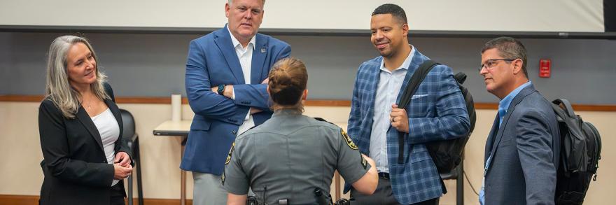 FirstNet Authority staff and Coverage Enhancement Workshop participants, including a uniformed law enforcement officer, stand in a circle speaking