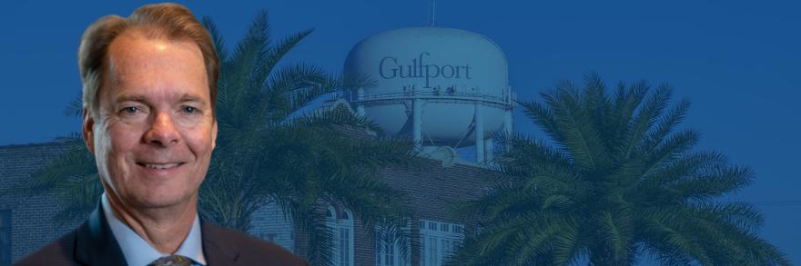 Mayor Billy Hewes’s headshot sits in front of a water tower with Gulfport written on it and foliage. 