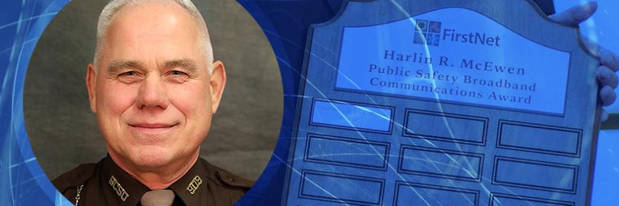 Sheriff Neil A. Miller and background of plaque for the Chief Harlin R. McEwen Public Safety Broadband Communications Award