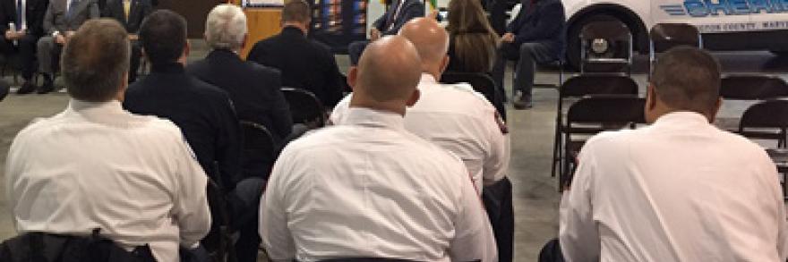 During an event marking one year of FirstNet in the State of Maryland, Sheriff Mullendore speaks at a podium in front of police vehicles