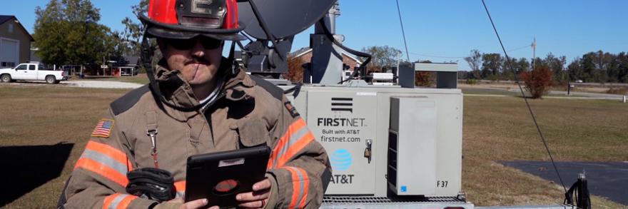 Firefighter using smart device in front of FirstNet deployable tower