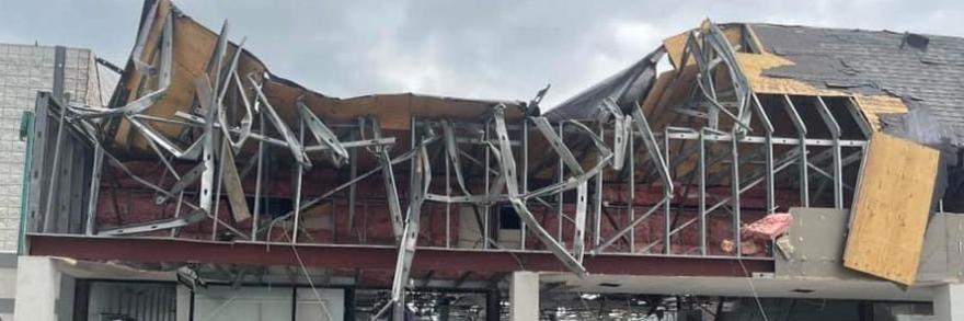A person looks up at commercial building with the roof and storefront caved in from a tornado in Otsego County